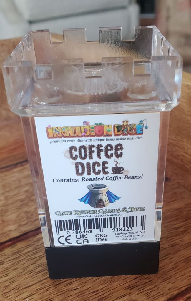 Image is a plastic tower. Inside the tower is a dice set. On the label, it says "Coffee Dice Contains: Roasted Coffee Beans".