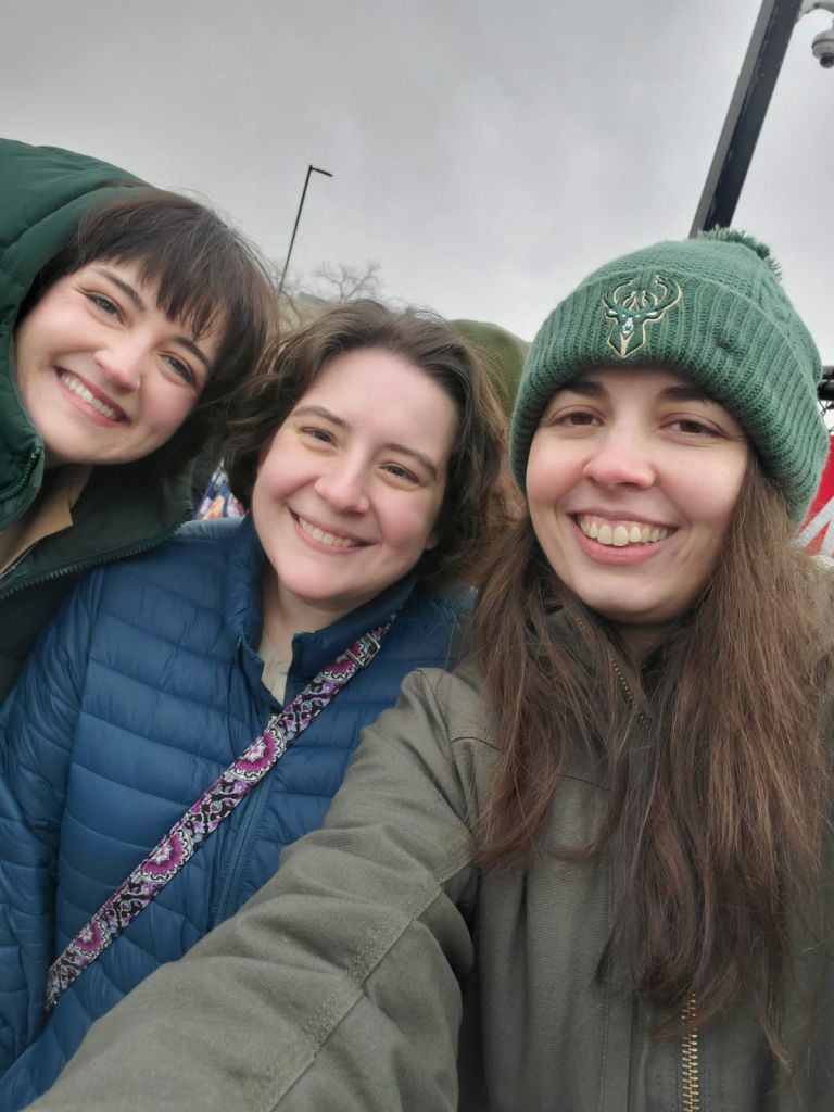 Image is a selfie of three women. We are smiling at the camera in the cold while waiting in line. Photo was taken outside of Inbound.