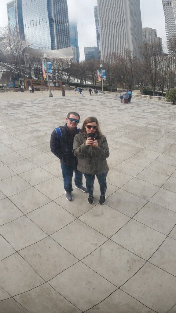 Image is a photo of me and my husband smiling into The Bean and taking a photo of our reflection.
