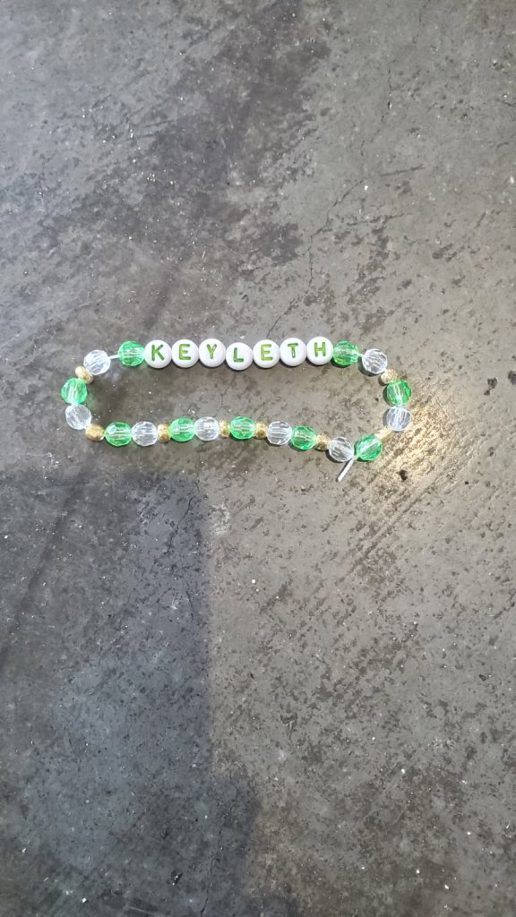 Imge is a photo of a charm bracelet on the floor. There are green and silver beads with the following letter beads "Keyleth" 