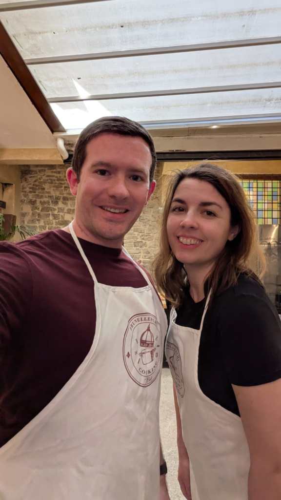 Image is a photo of me and my husband smiling in our aprons before the cooking class began. 
