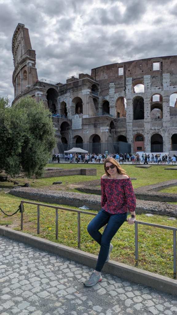 Image is a phot of me sitting on a bar with the colosseum in the background. I'm smiling at the camera wearing sunglasses. 