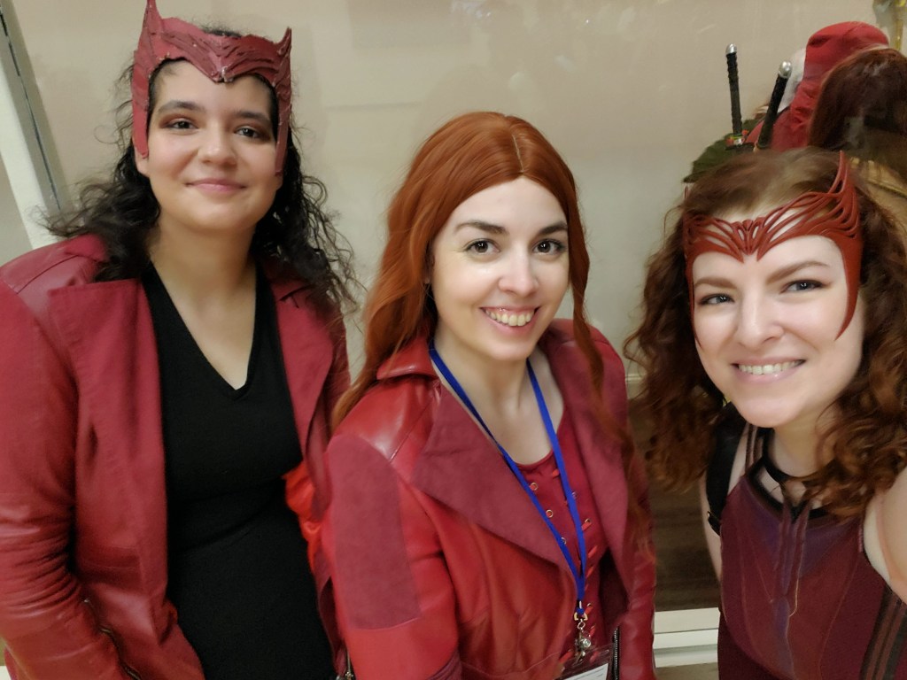 Image is a photo of three women in Scarlet Witch cosplays. We are smiling at the camera. 