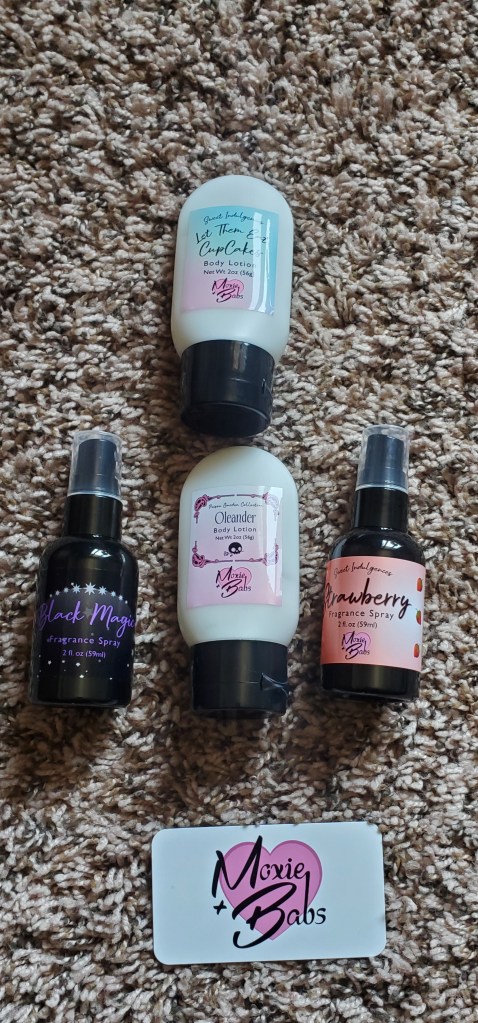 Image is a photo of two small lotions and two fragrance sprays. The business card is white. It says "Moxie + Babs" with a pink heart on the background. 