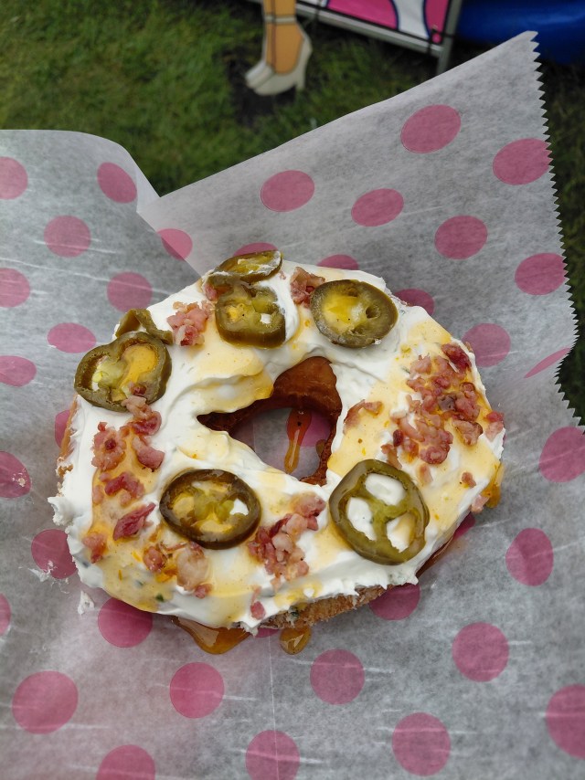 Image is a photo of a doughnut with jalopenos on it. It has honey and bacon on it too. 