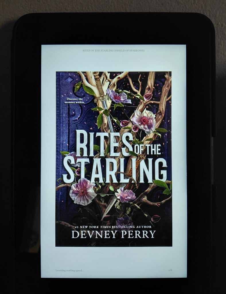 Image is a photo of a book cover loaded on a Kindle. The book is called Rites of the Starling by Devney Perry. It shows brown branches with various swords on top of them. There are leaves and bright pink flowers. Off to the left it says "Discover the Monster Within" 